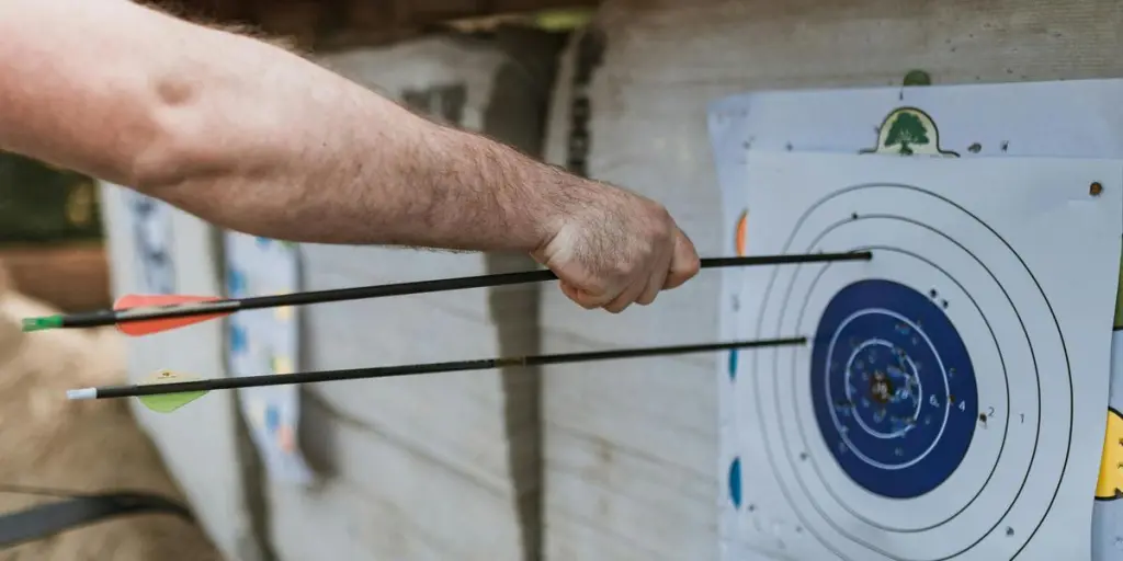 Un brazo enfocado que sostiene flechas cerca de un objetivo en un entorno de práctica de tiro con arco.