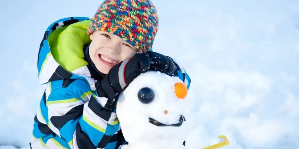 Une image horizontale d'un jeune garçon avec un drôle de bonhomme de neige