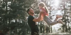 Um momento de alegria entre um pai e uma filha brincando em uma floresta ensolarada, capturando amor e felicidade