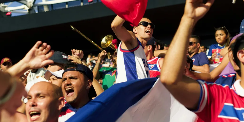 Un animado grupo de aficionados al fútbol celebrando enérgicamente con banderas y aplaudiendo en un estadio.