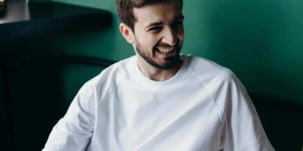 A man with a warm smile wearing a white t-shirt in a cozy home environment