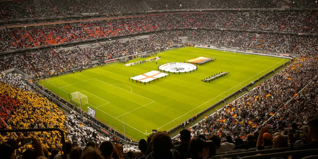 Un estadio repleto de fanáticos viendo un partido de fútbol en vivo, con colores vibrantes de la multitud.