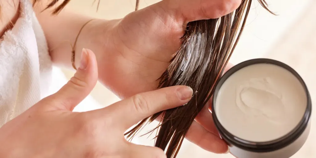 A person applying a hair treatment cream to their hair