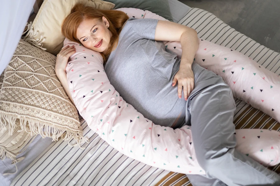 A pregnant woman smiling on a c-shaped pillow