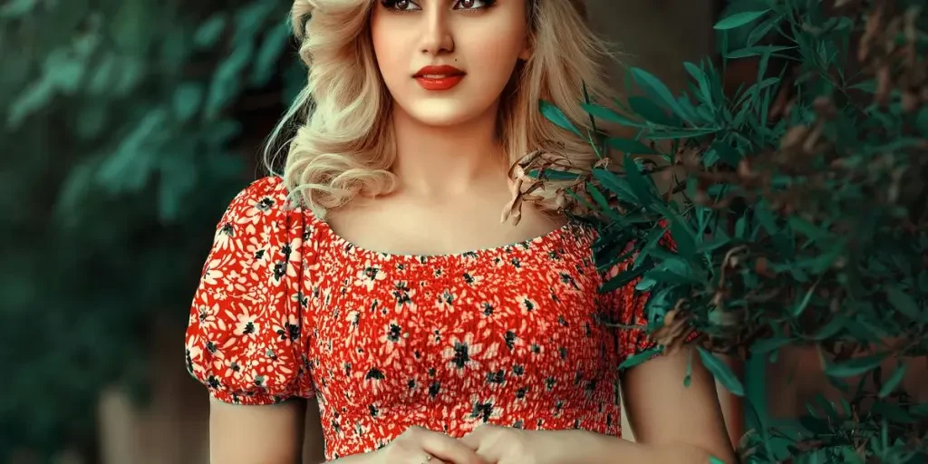 A stylish woman in a red floral dress standing amidst lush green foliage