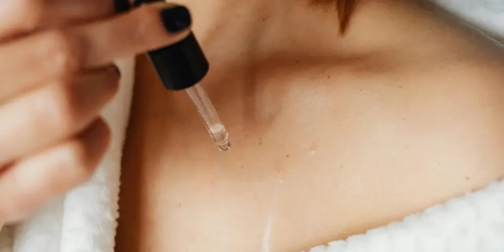 A woman applying skin care oil to her collarbone area for self-care treatment by Photo