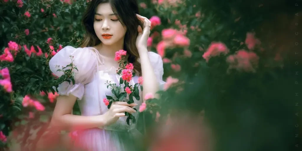 A woman gracefully poses amidst vibrant flowers in a serene summer garden