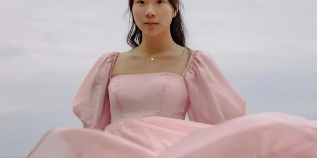 A woman in a pink puff sleeve dress stands against a serene seascape backdrop