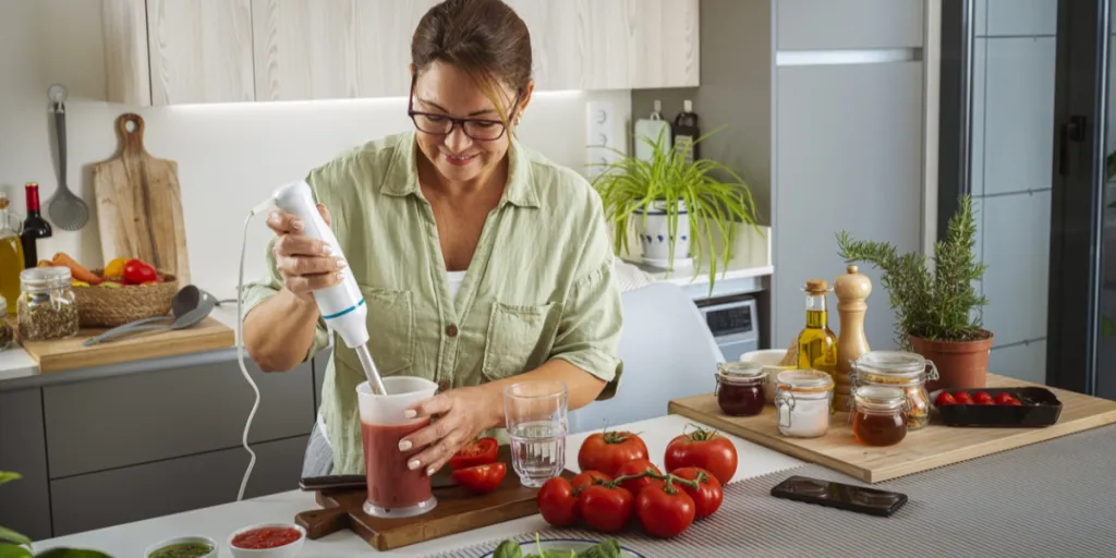 Une femme prépare du jus de tomate avec un mixeur plongeant