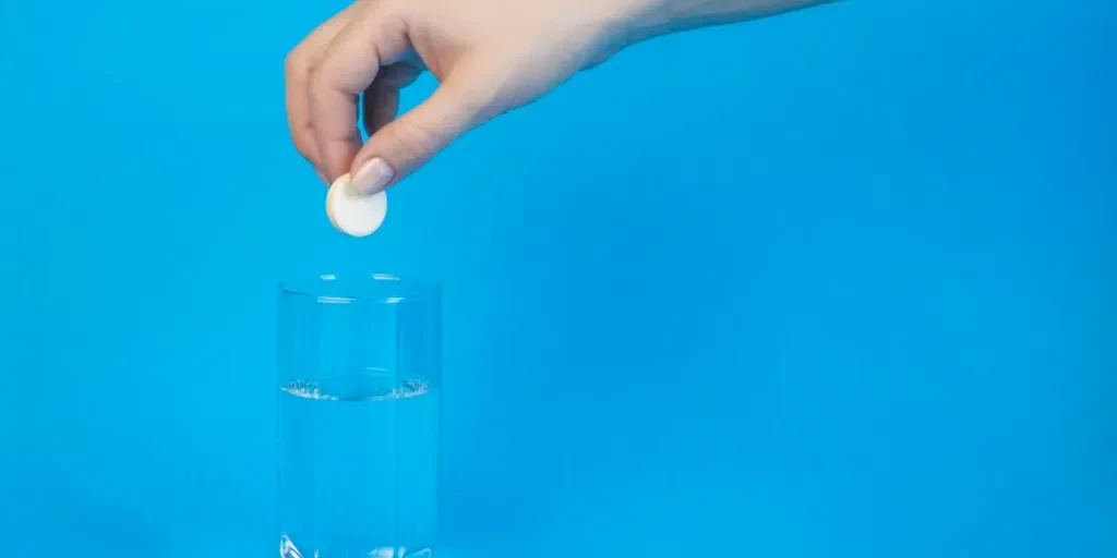 La mano di una donna getta una pillola effervescente in un bicchiere d'acqua su uno sfondo blu