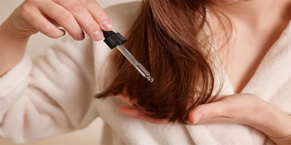 Une jeune femme applique une goutte d'huile à l'aide d'une pipette sur ses cheveux