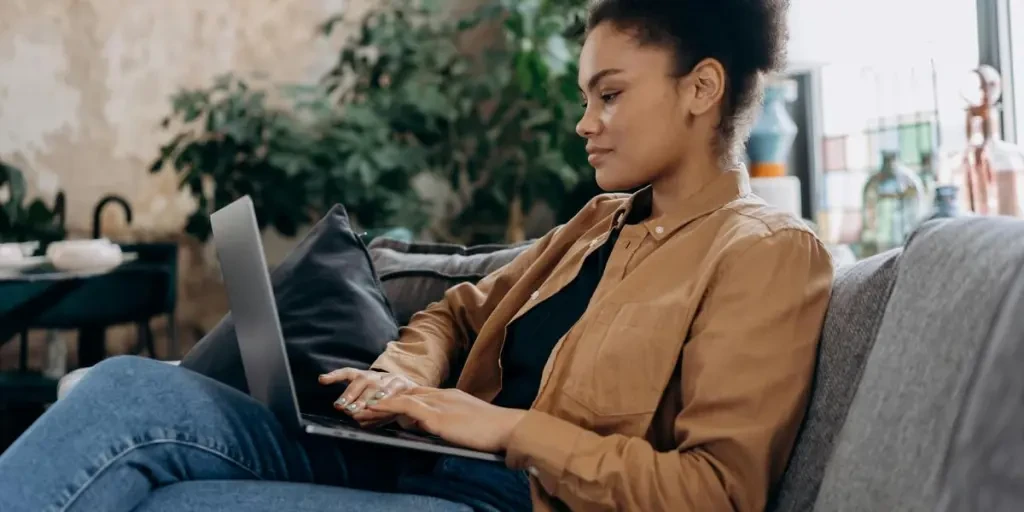 A young woman in casual clothing works on her laptop in a cozy home office setting