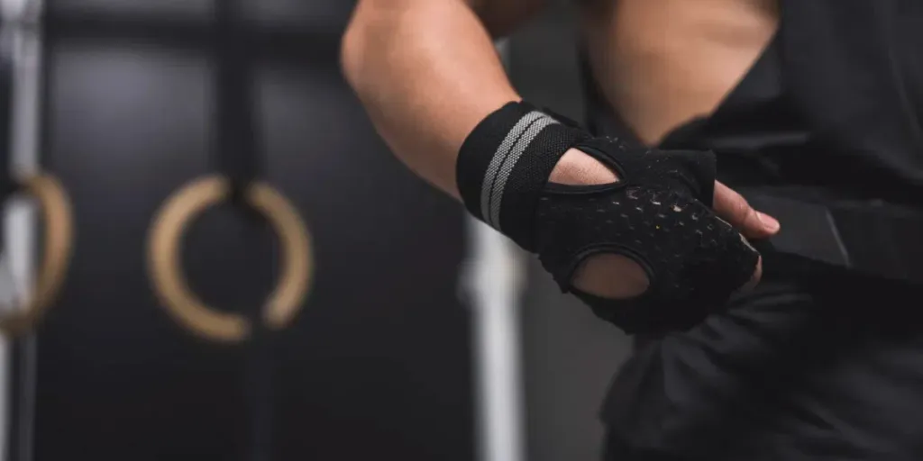 An anonymous man wearing and tank top and training gloves tightening