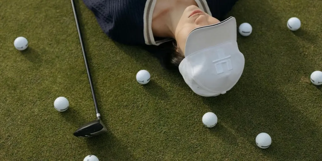 Femme asiatique portant une casquette blanche allongée sur un terrain de golf avec des balles de golf et un club