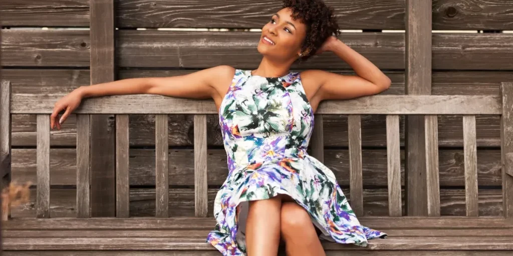 Attractive African American woman sitting on wooden bench wearing a sundress