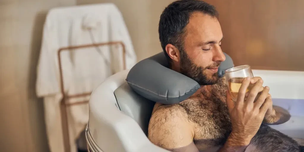 Bearded gentleman enjoying delicious drink while relaxing in bathtub