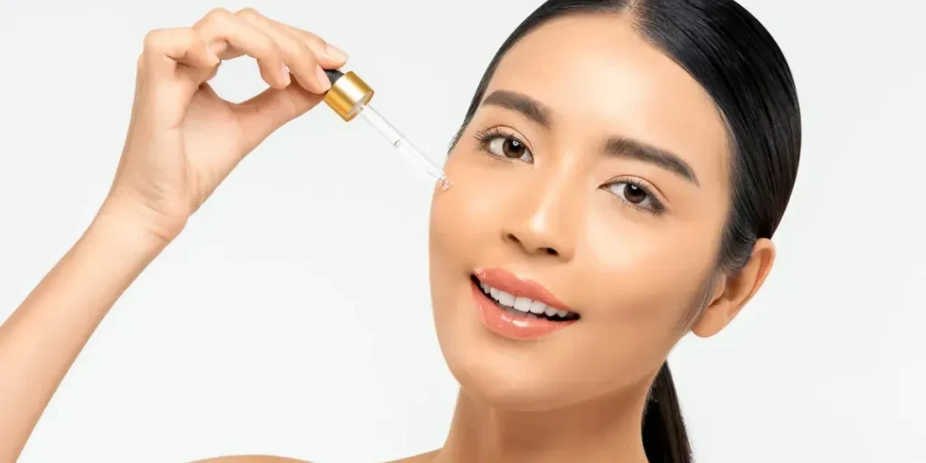 Beautiful Asian woman applying anti aging moisturizing serum on her face for beauty and skin care concepts