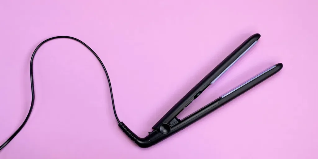 Black corded hair straightener isolated on pink background