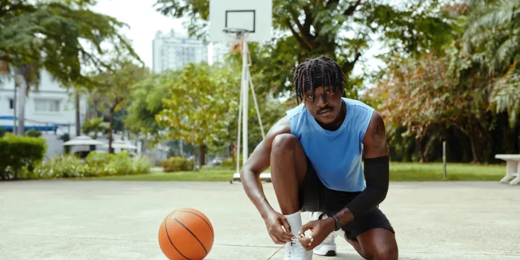 Jugador de baloncesto callejero negro atándose los cordones de los zapatos mientras se prepara para el partido