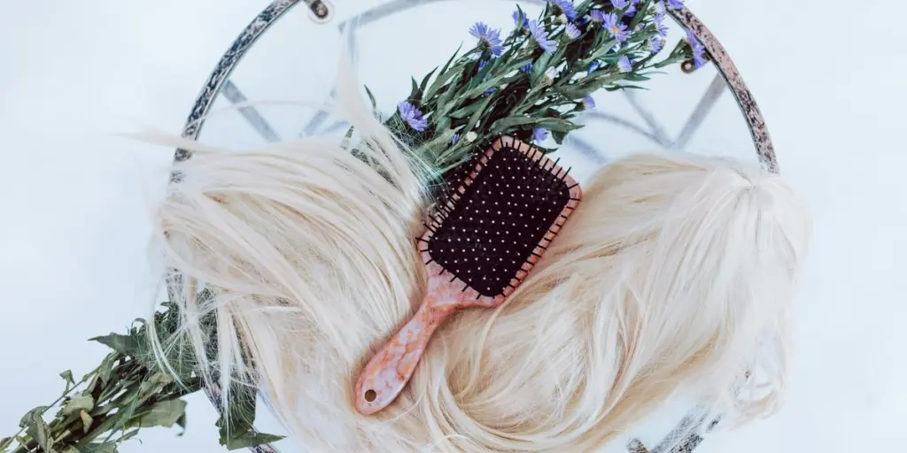 Blonde wig styled with brush and purple flowers on a round table, showcasing hair beauty and caret