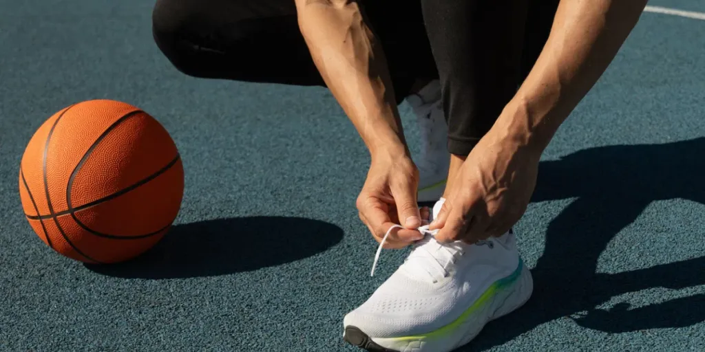 Primer plano de un jugador de baloncesto atándose los zapatos deportivos en una cancha de baloncesto al aire libre. Últimos preparativos