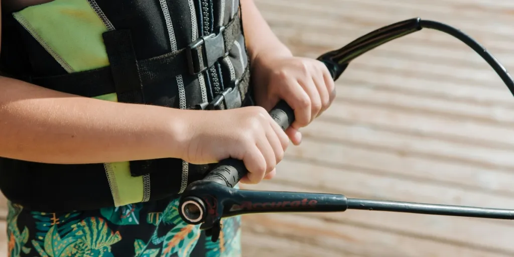 Close-up van een kind dat een wakeboardhandvat vasthoudt op een zonnige dag aan het meer