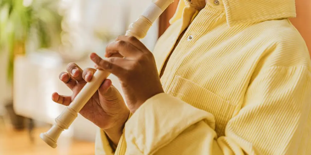 Close-up of a child in yellow playing a recorder indoors with natural light