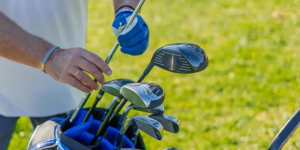 Nahaufnahme der Hände eines älteren Golfers, der sorgfältig einen Schläger aus seiner Golftasche auswählt