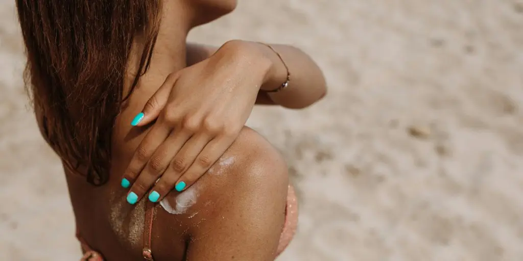 Close-up de uma mulher aplicando protetor solar no ombro em um dia ensolarado de praia no verão