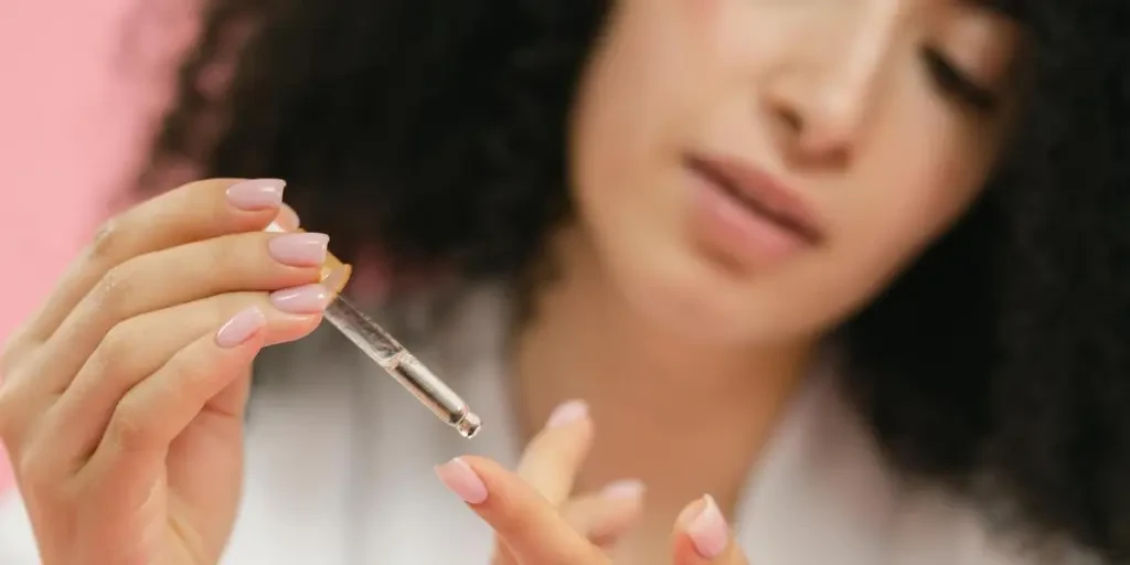 Close-up of a young woman applying skincare serum with a pipette against a pink background