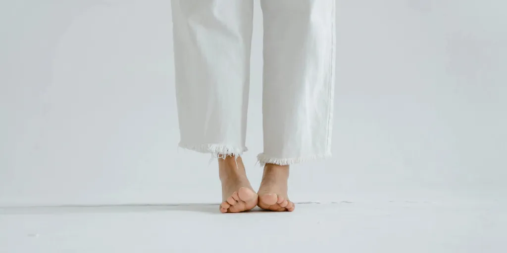 Close-up of bare feet in white jeans on a white minimalist background by Tima Miroshnichenko