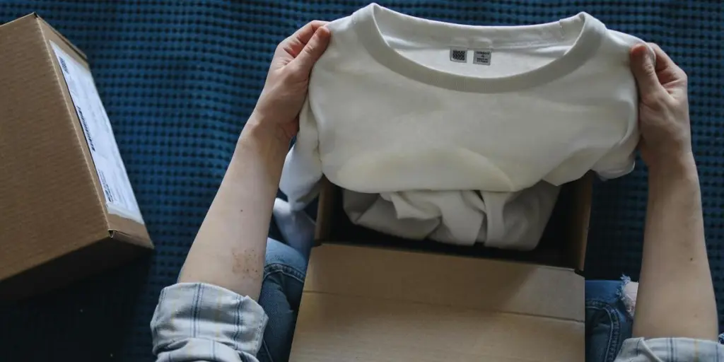 Close-up of hands opening a package containing a new white t-shirt indoors