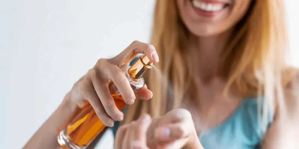 Close-up wanita muda yang tersenyum mengoleskan parfum di pergelangan tangannya sambil berdiri di rumah
