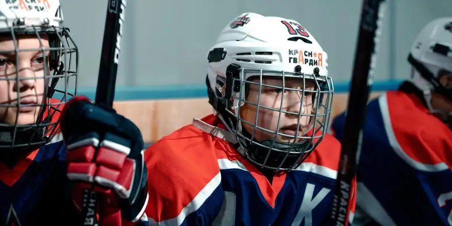 Primo piano di giovani giocatori di hockey su ghiaccio con mazze e caschi, pronti per una partita sulla pista