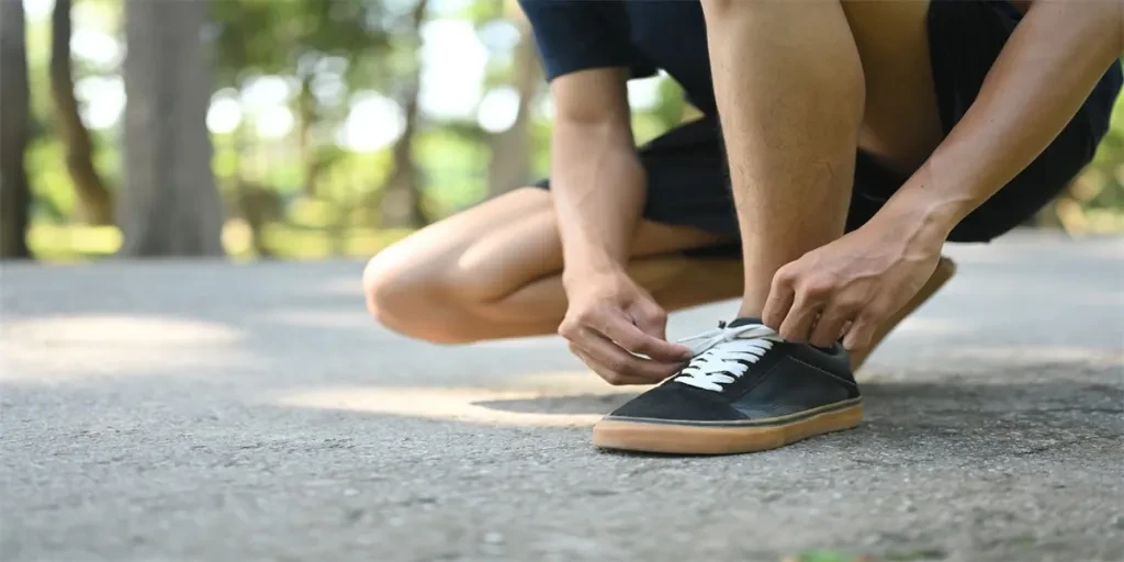 Close up young athlete tying shoelaces on pathway preparing for run in a green park