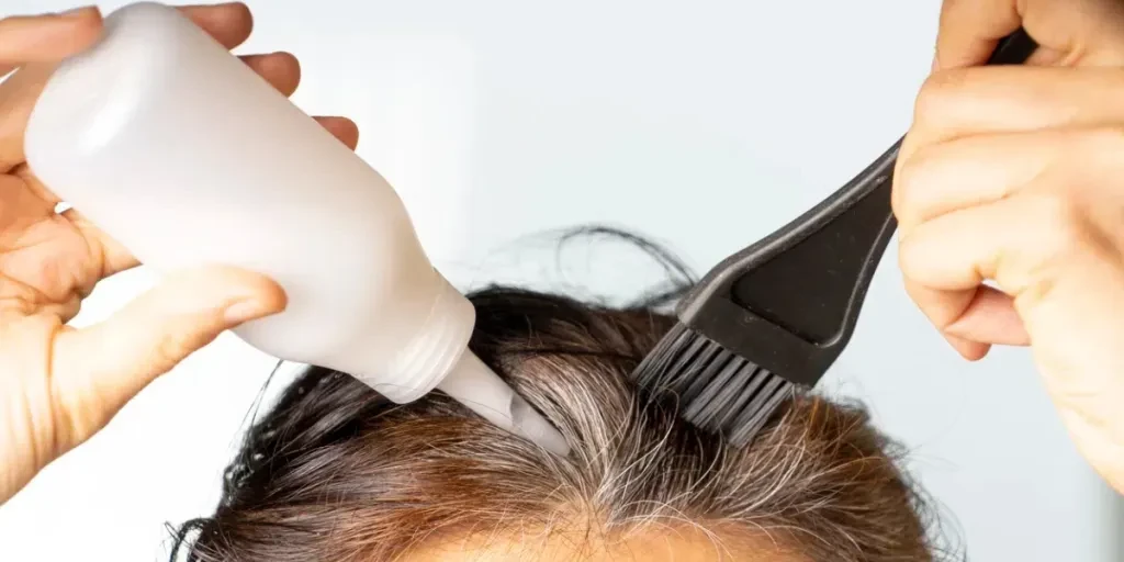 Mani della donna del primo piano che tingono i capelli usando la spazzola nera