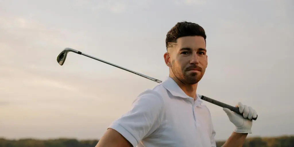 Confident male golfer posing with club at sunset, exuding style and skill