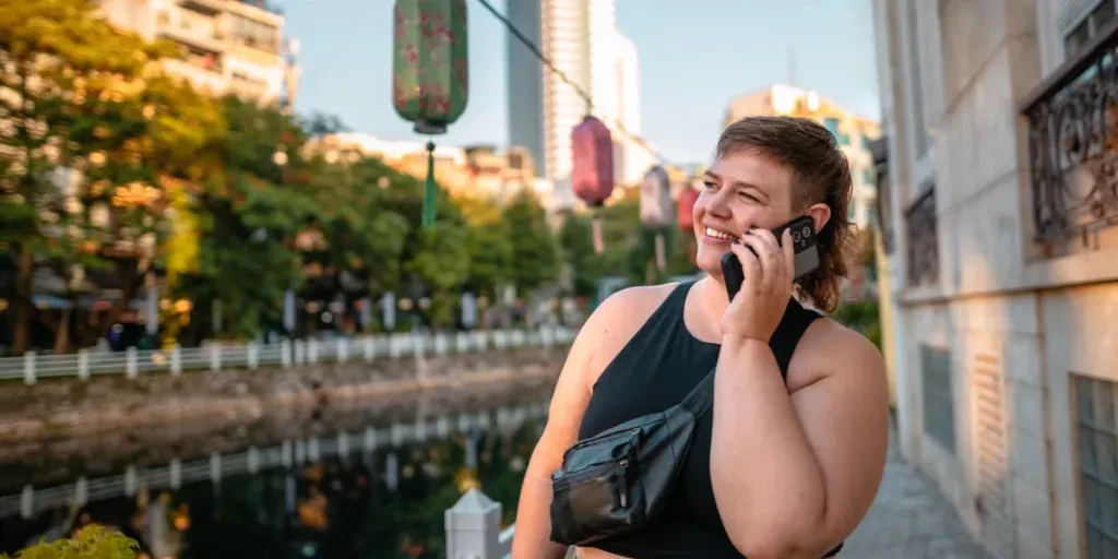 Mujer joven segura de sí misma hablando por teléfono al aire libre junto al lago Truc Bach en Hanoi