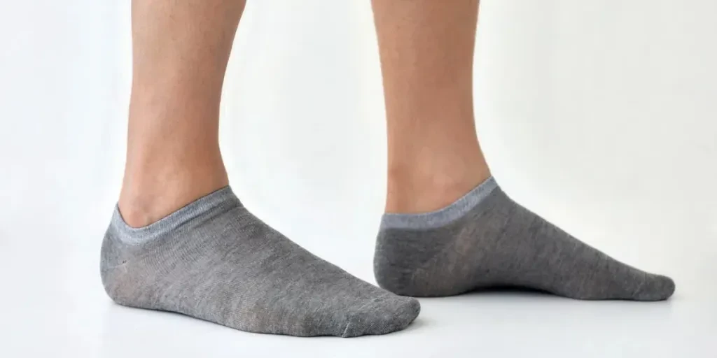 Crop anonymous male wearing gray socks standing against white background in light studio