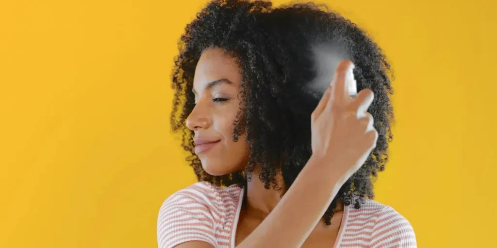 Fotografía recortada de una mujer joven rociándose el cabello con laca