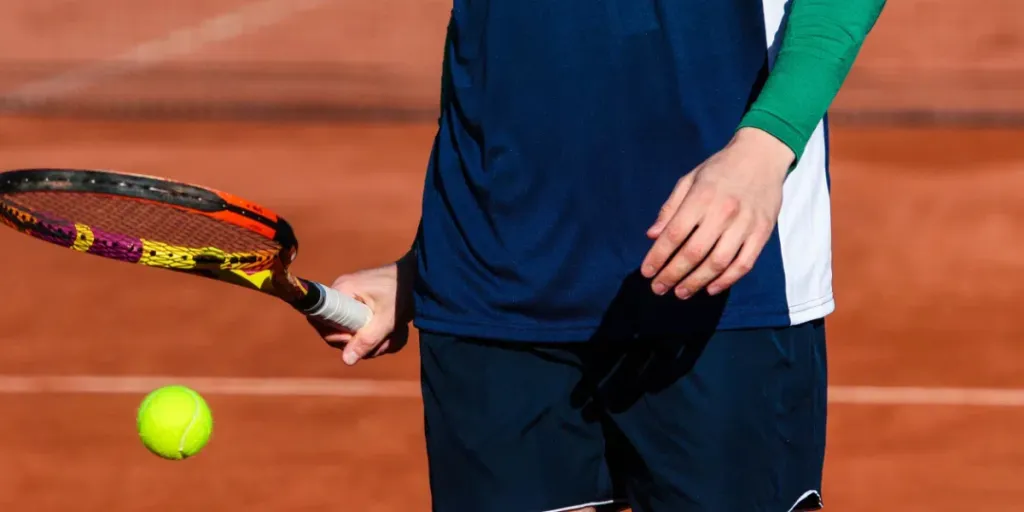 Particolare di un ragazzino con la racchetta che gioca a tennis su un campo in terra battuta durante un torneo universitario