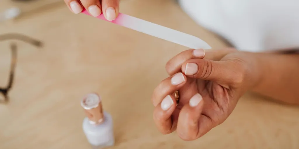 Detailed view of hands filing nails with a nail polish bottle nearby, showcasing personal grooming by Photo