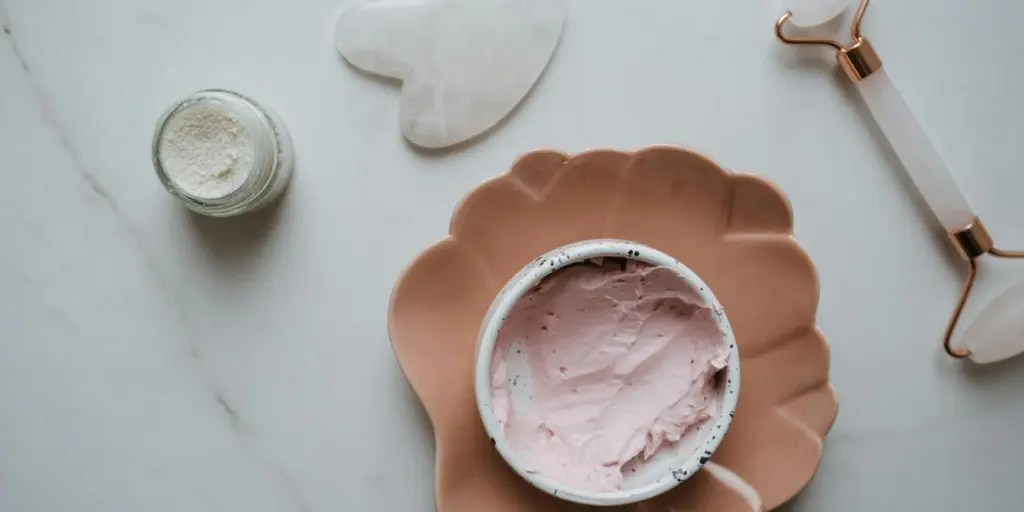 Elegante vista dall'alto di prodotti essenziali per la cura della pelle, tra cui crema, gua sha e rullo su superficie in marmo, perfetti per concetti di bellezza