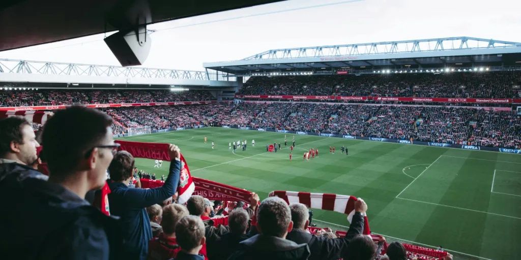 Fans juichen als spelers het veld opkomen in een levendig voetbalstadion, wat een elektrische sfeer creëert