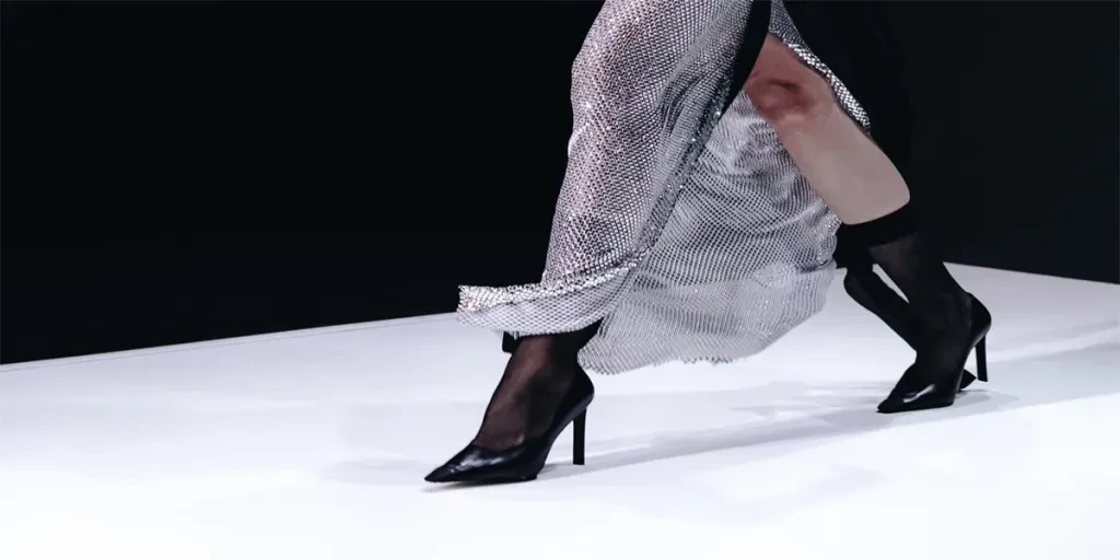 Fashion details of a long silver skirt and black high heels on a black white background