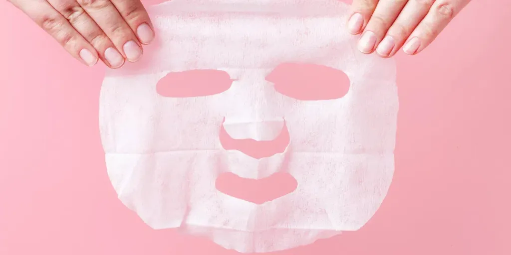 Female hands hold white fabric mask on a pink background