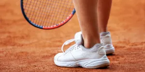 Beine einer Tennisspielerin in Tennisschuhen stehen aus nächster Nähe auf einem Sandplatz