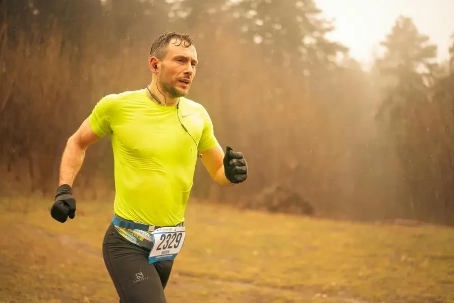 Homem adulto em forma correndo em uma corrida de cross country usando roupas esportivas neon e luvas, capturado em movimento ao ar livre em Brașov