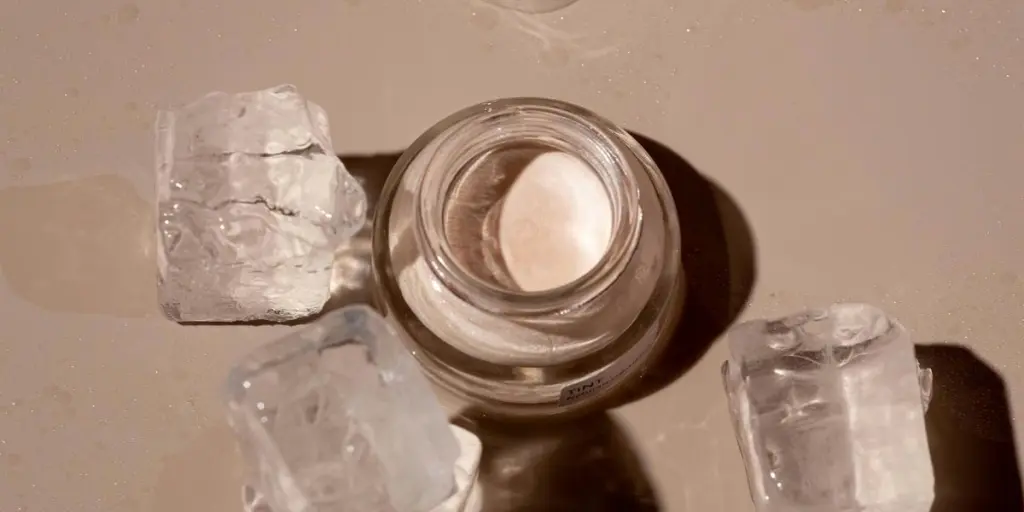 Flat lay of a skincare product surrounded by ice cubes on a textured surface