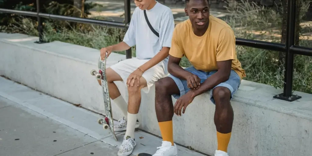 Amigos multirraciais jovens de corpo inteiro com skates vestindo roupas casuais de verão sentados na passarela em um parque exuberante